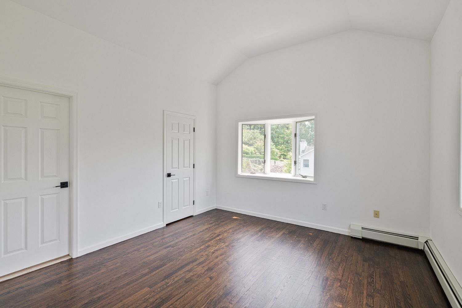 Empty room with dark wood floor, white walls, two doors, and a window.
