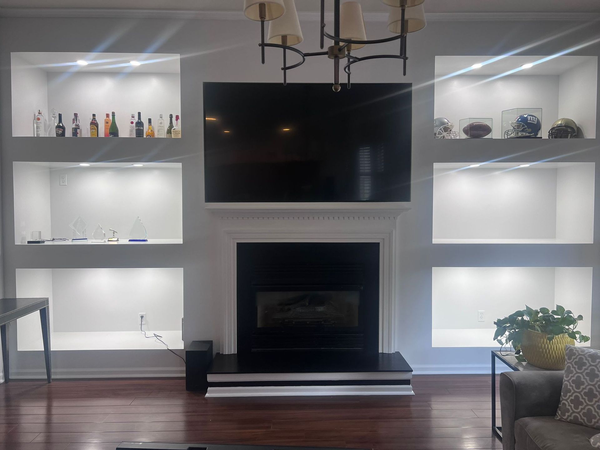 Fireplace with TV, built-in lit shelves, and bottles/decorations. Room with hardwood floor.