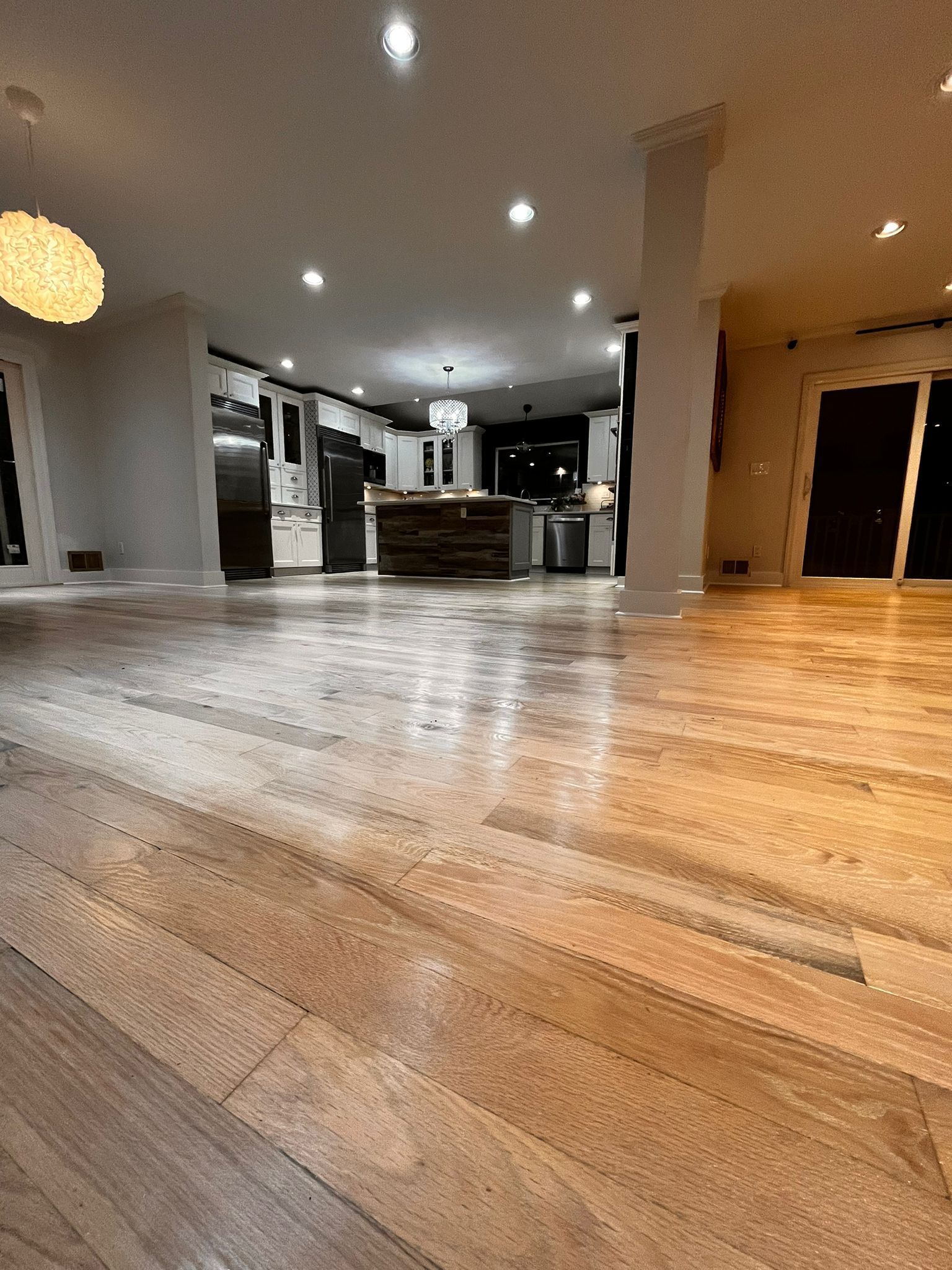 Wide shot of a well-lit kitchen with hardwood floors; island in center, appliances in background.