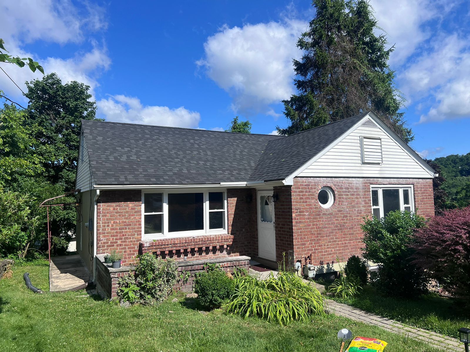 Brick house with dark roof, white trim, small porch, and landscaping under a blue sky.