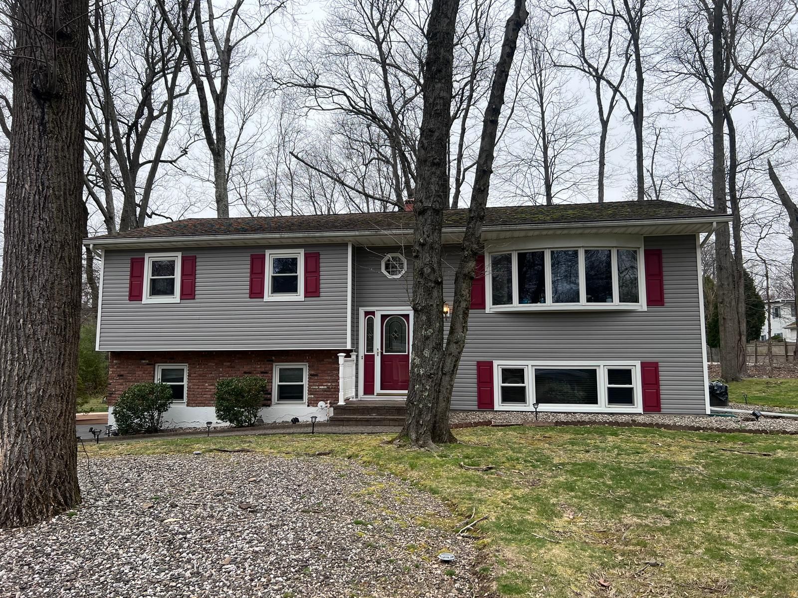 Gray house with red shutters and door, brick and gray siding, trees in front.