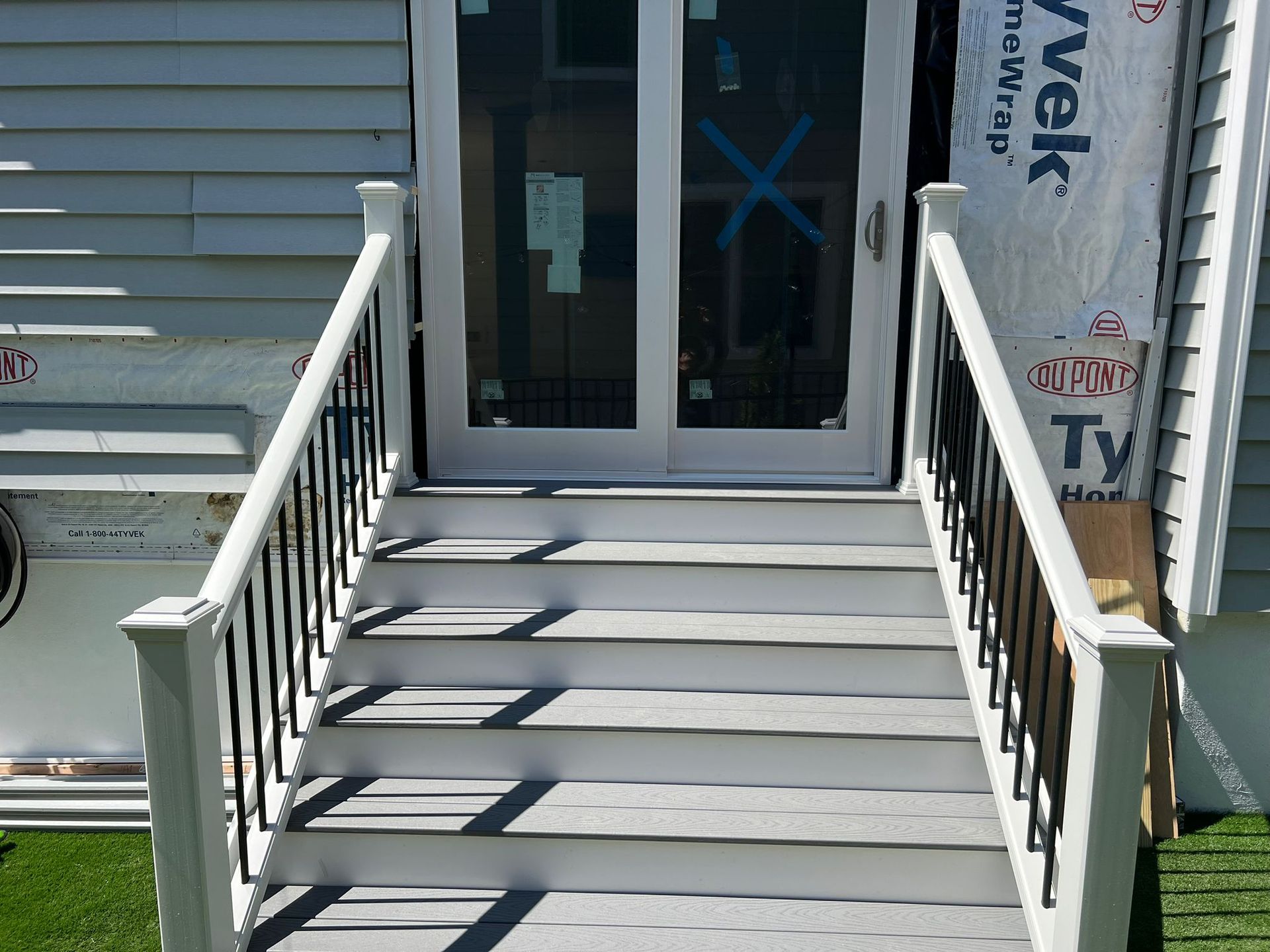Steps leading to a white door, white railings with black spindles. Gray steps, light blue house siding.
