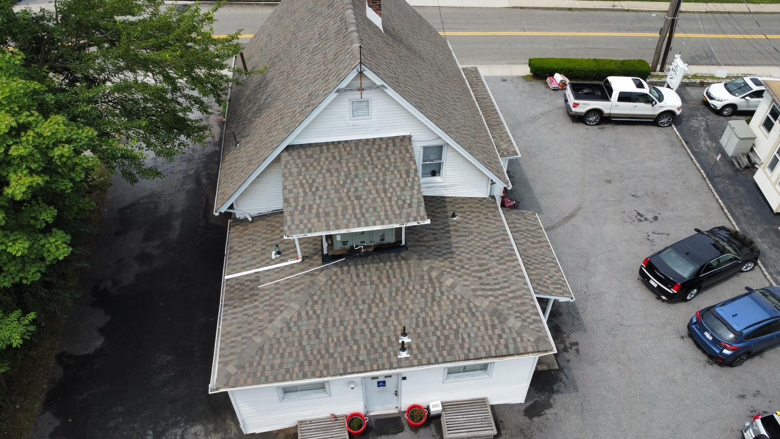 White building with gray roof; cars parked in lot next to it.