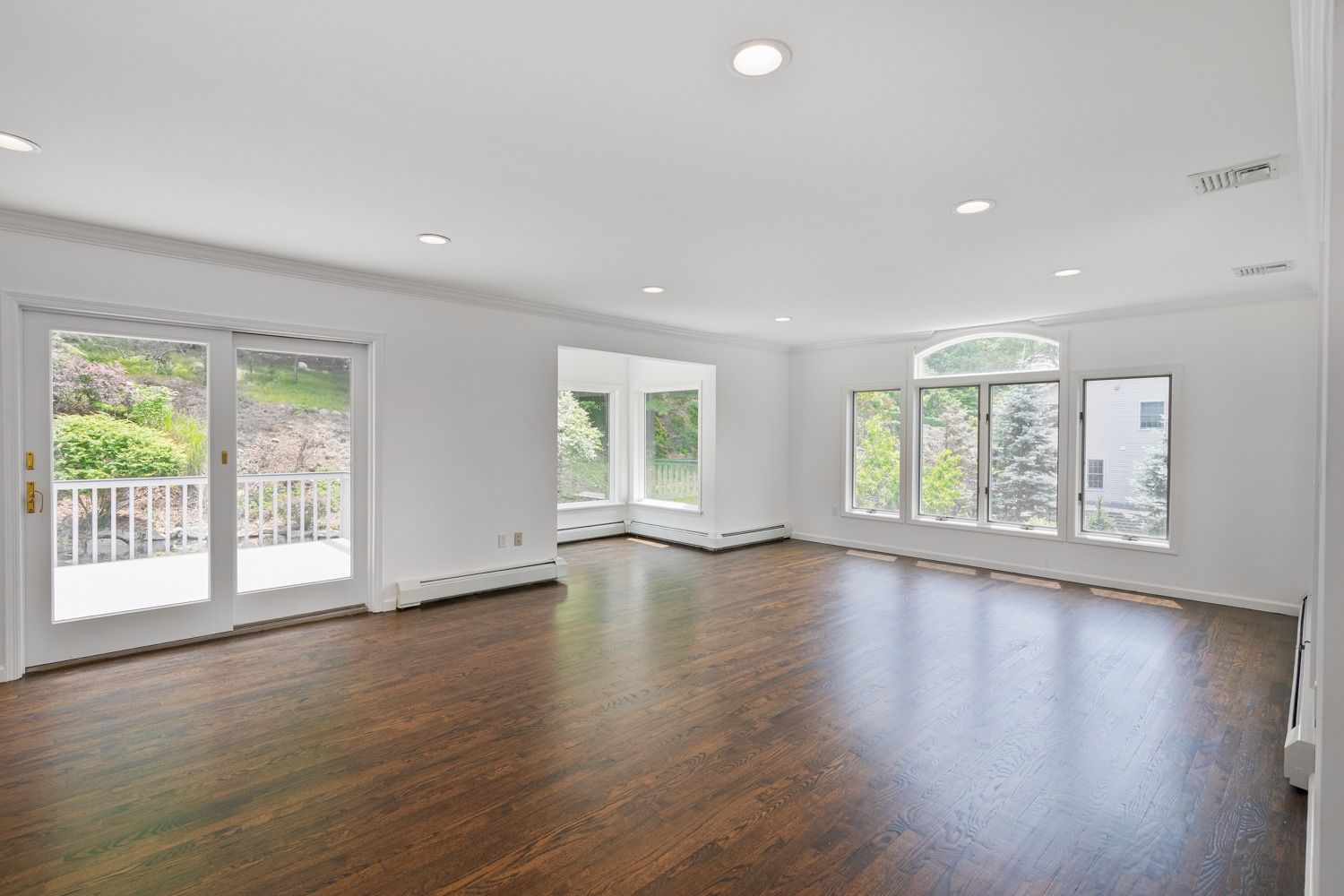 Empty, bright living room with dark wood floors, white walls, and large windows.