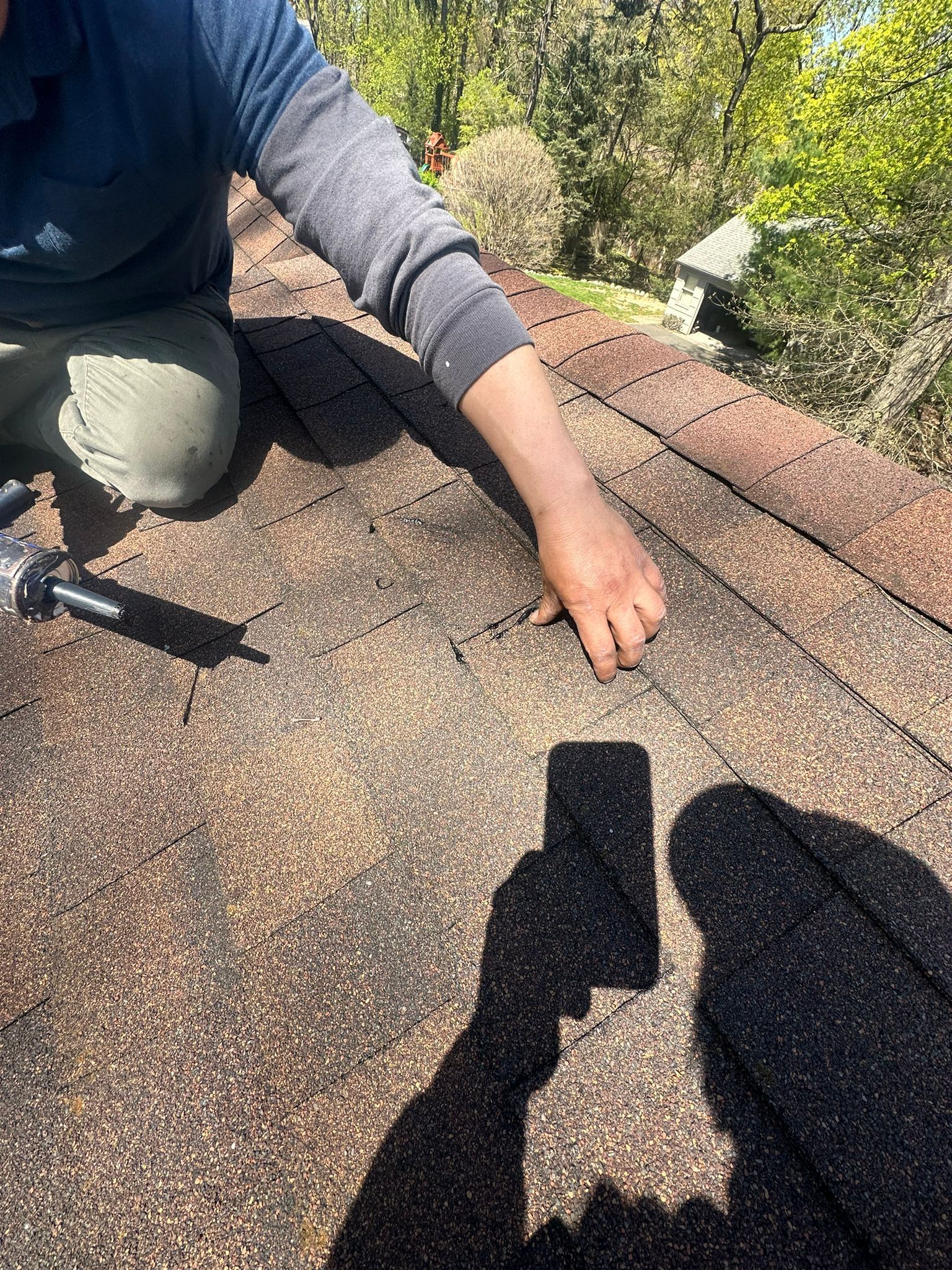 Person on a roof repairs shingles with a tool. Sunny day.