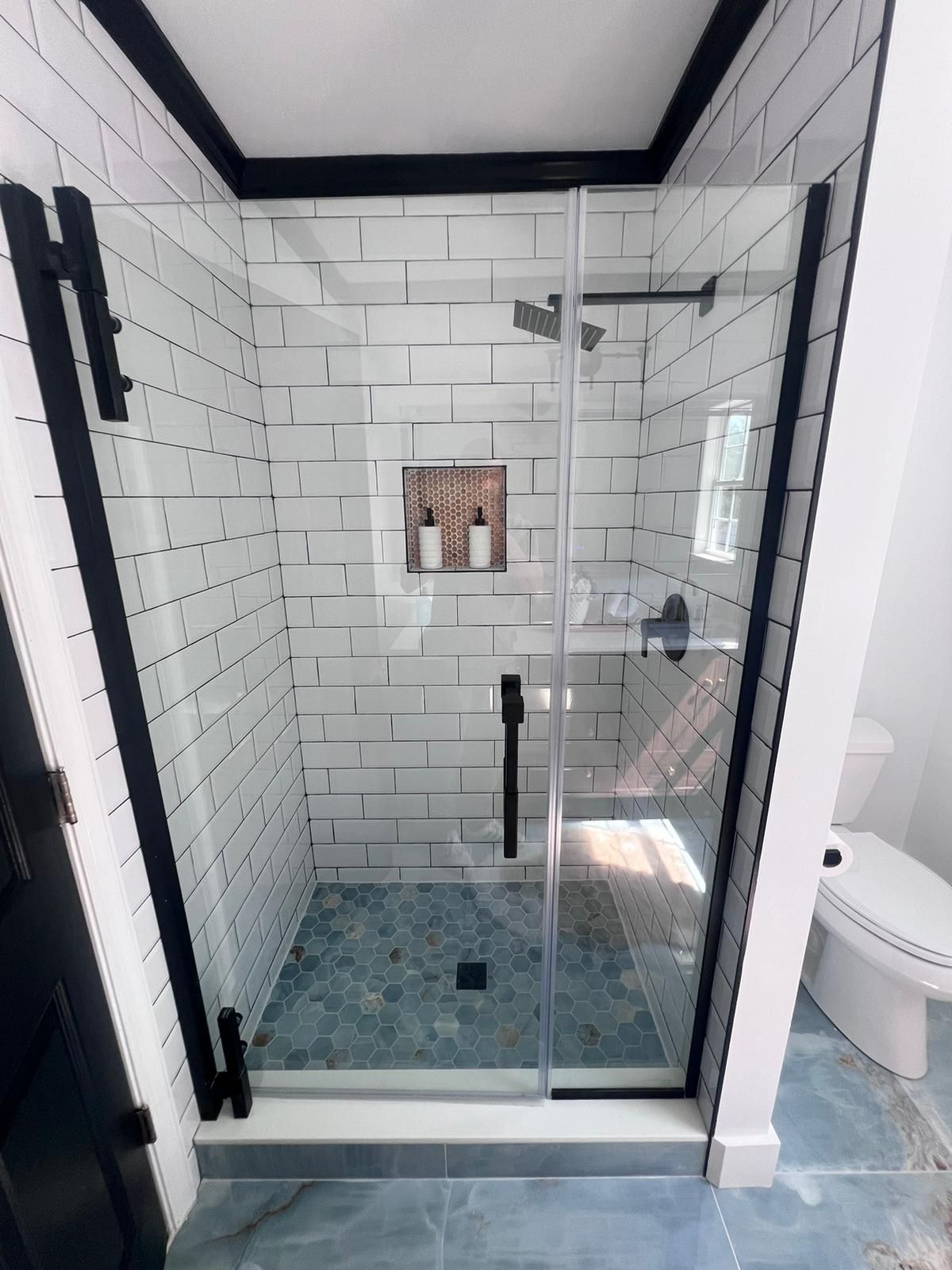 Shower with black trim and hardware, white brick tile walls, and blue tile floor.