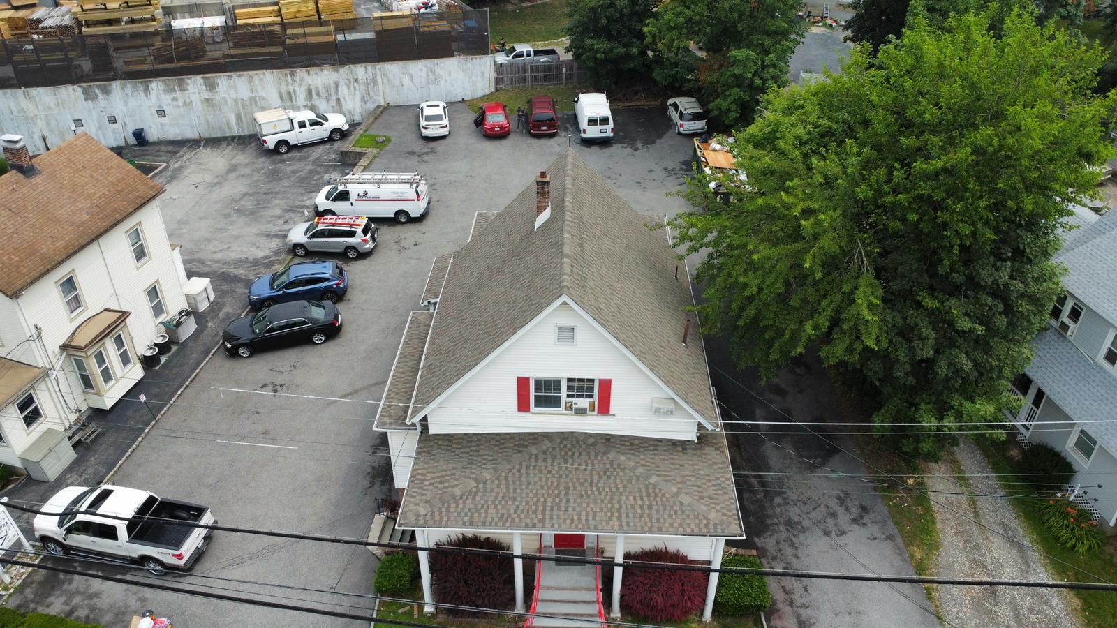 Aerial view of a building with a brown roof and red shutters; cars parked around it.