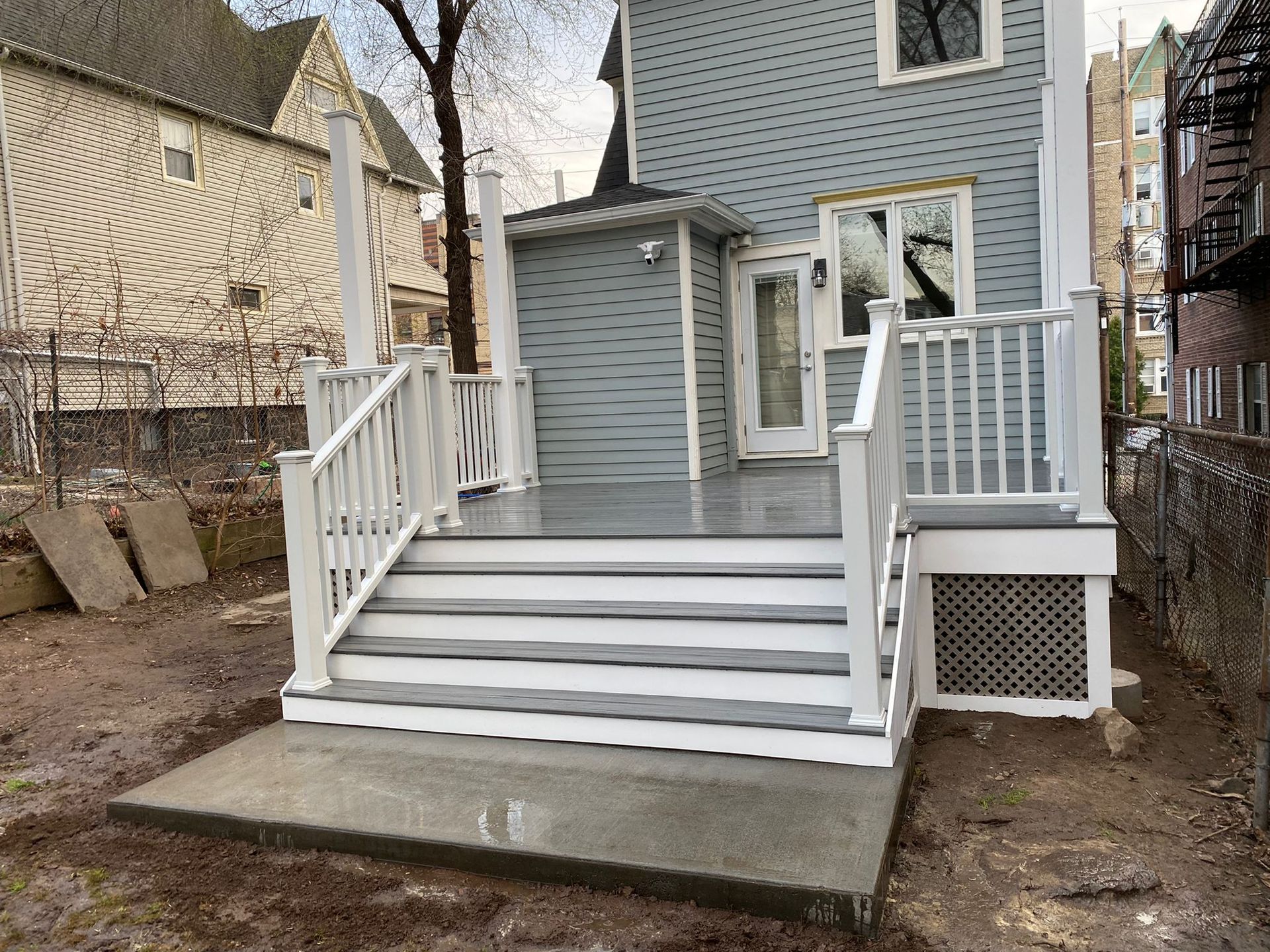 New wooden deck with white railings and gray steps leading to a light blue house.