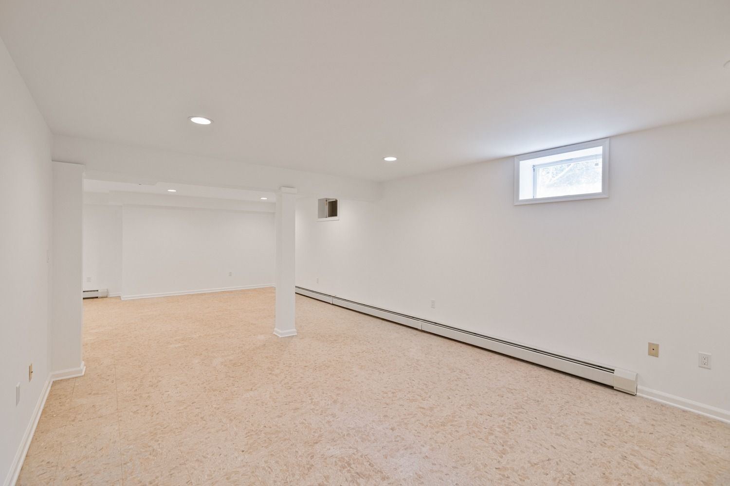 Empty, bright basement with beige carpet, white walls, and a small window.