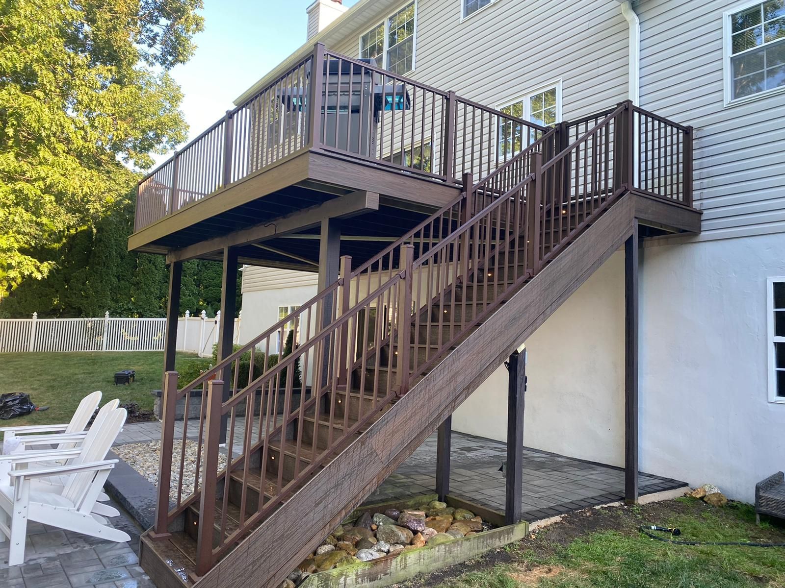 Brown composite deck with stairs leading to a two-level structure attached to a house.
