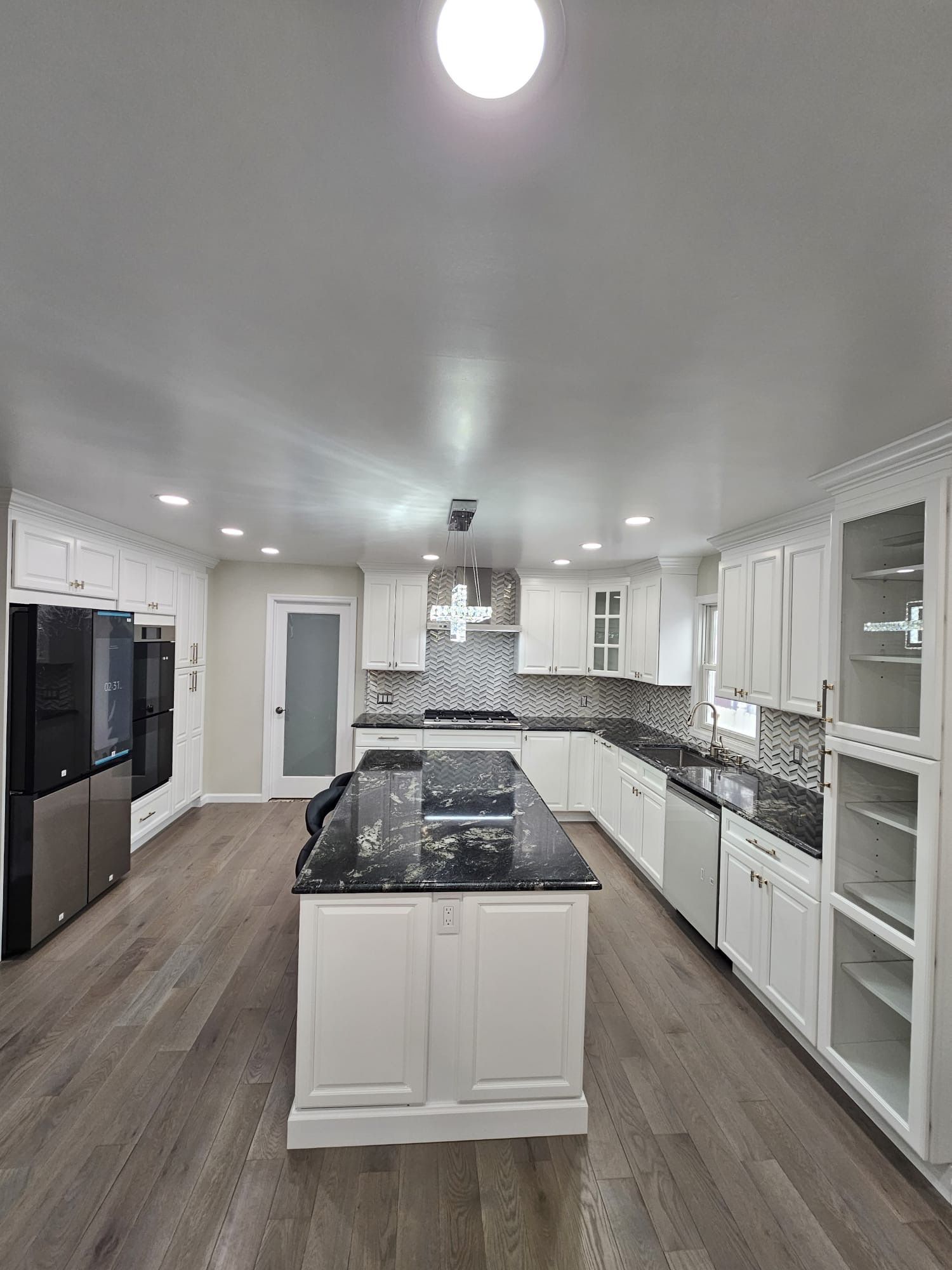 White kitchen with dark countertops and island; hardwood floor.