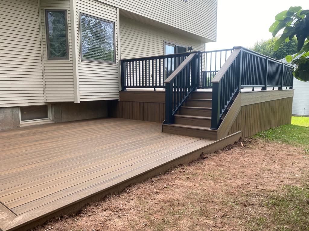 Brown composite deck with stairs, black railing, beige siding, and green grass.