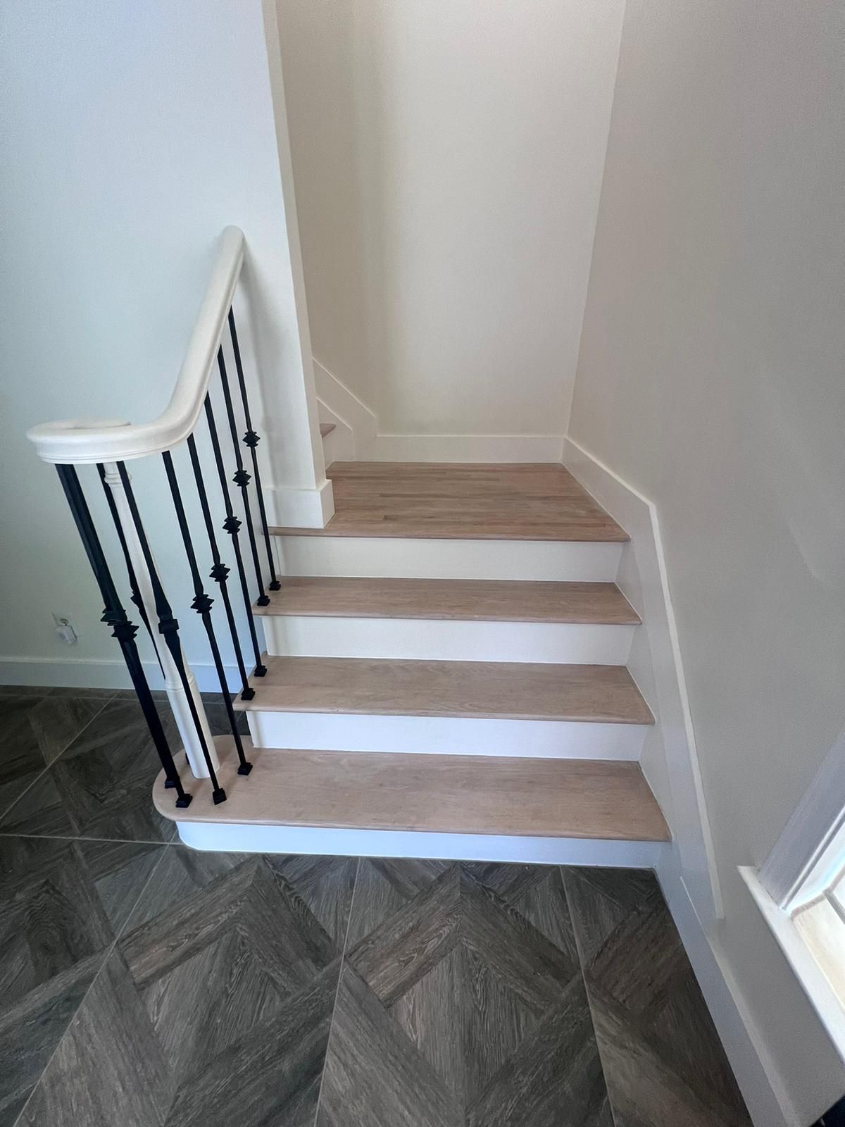 Staircase with wooden steps, white risers, black railing, and gray tiled floor.