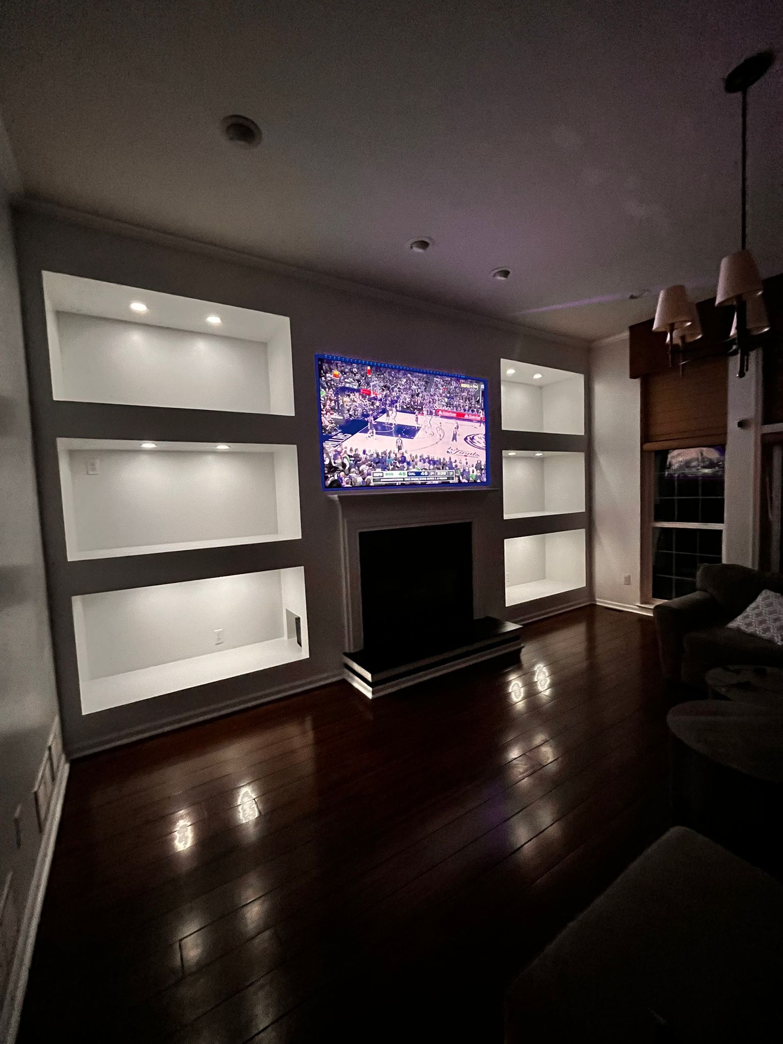 Living room with built-in shelves flanking a fireplace and TV; dark wood floors, warm lighting.