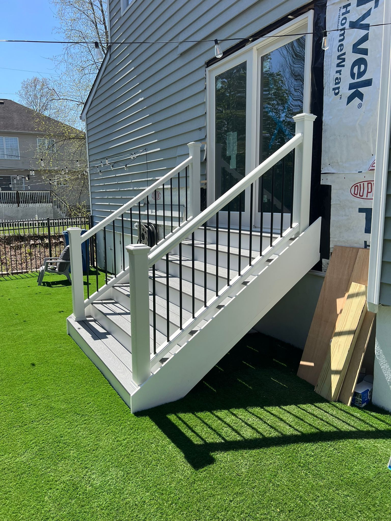 White deck stairs with black railing leading to a back door, on green turf.