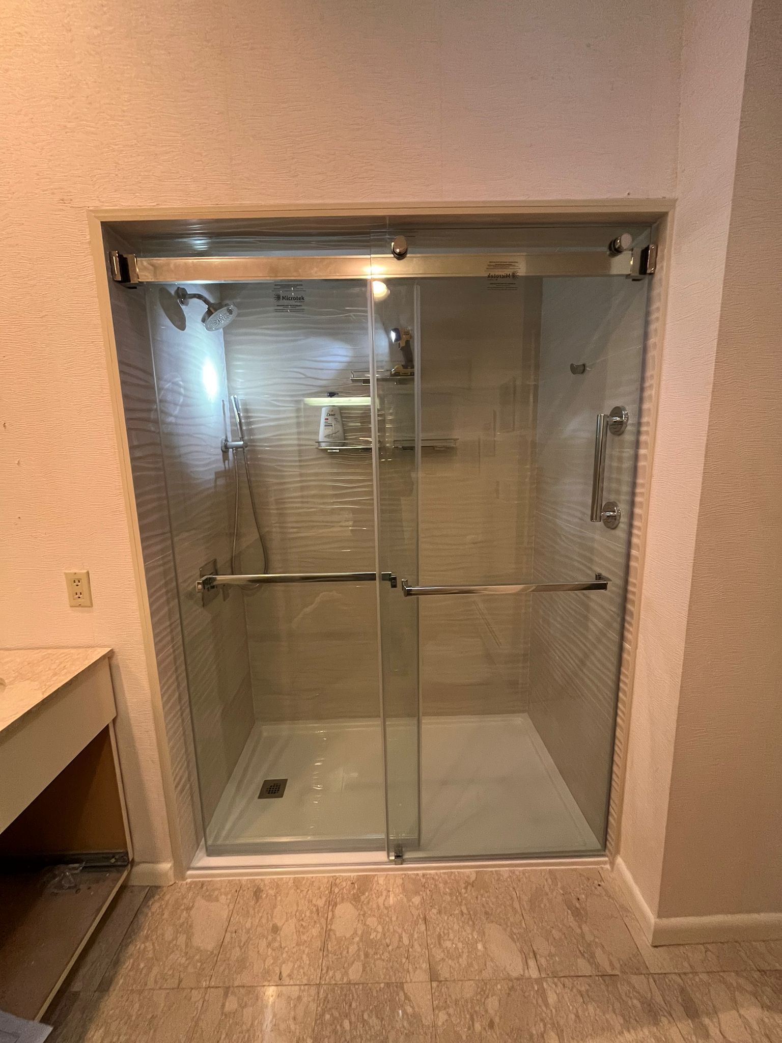 A modern shower with sliding glass doors, a white base, and metal fixtures in a neutral-toned bathroom.