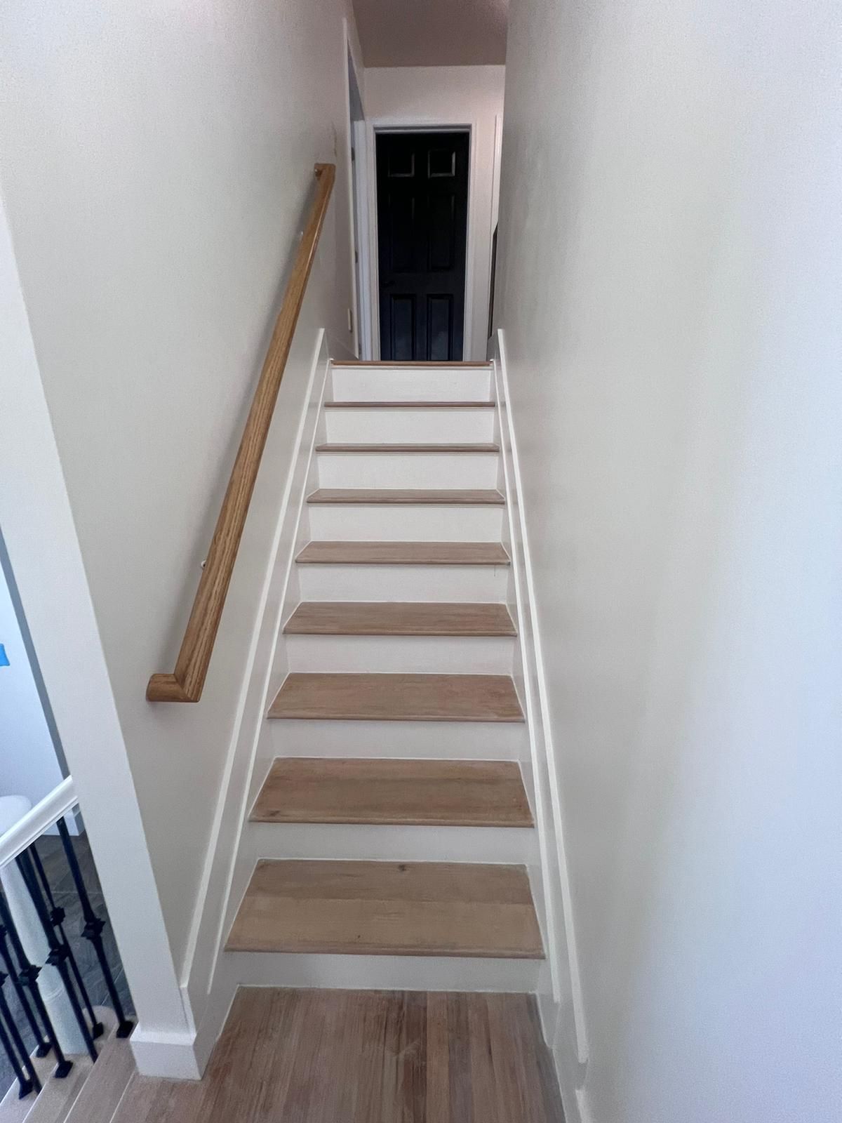 Staircase with wooden steps, white risers, and a wooden handrail leading upwards towards a dark door.