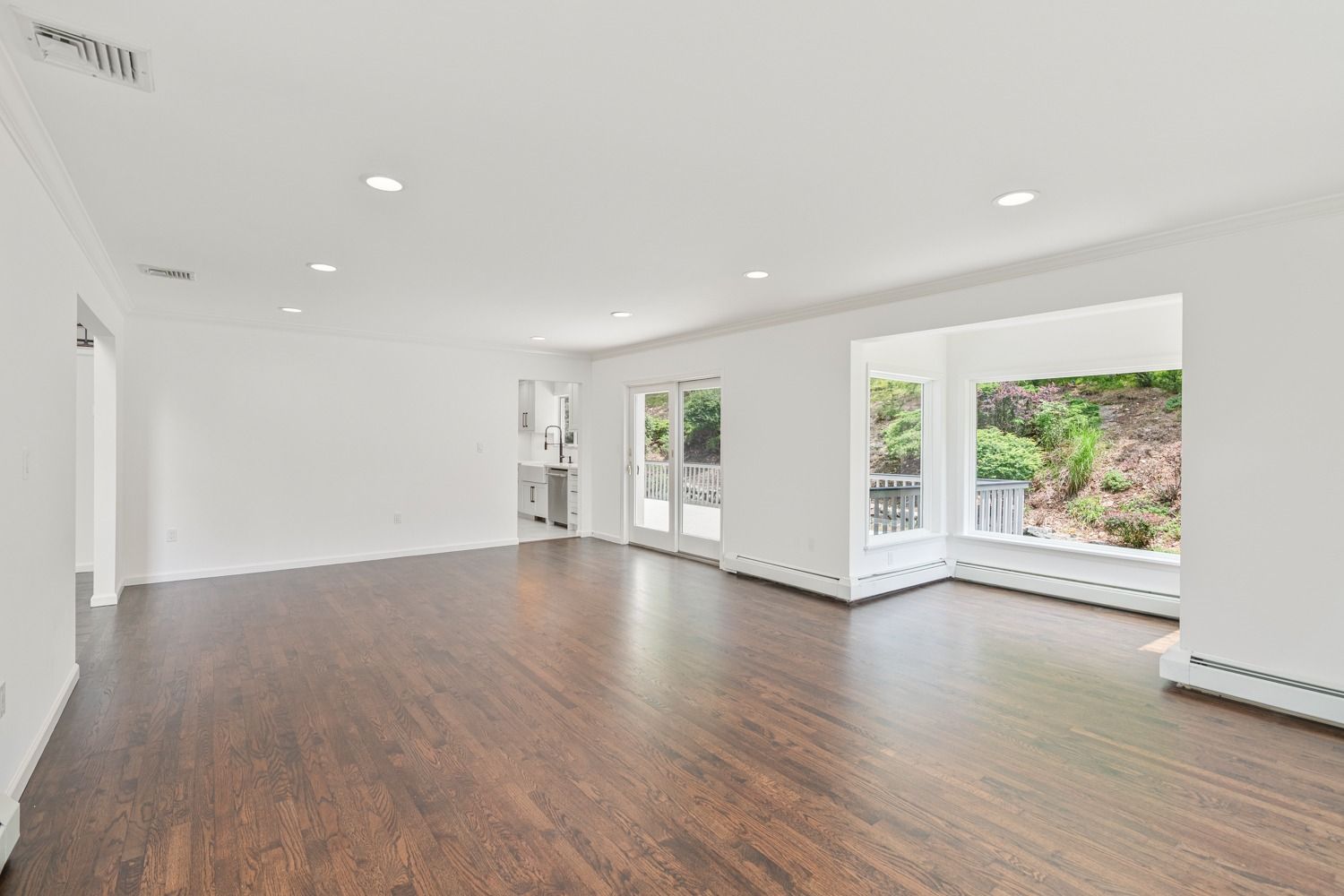Empty living room with dark wood floors, white walls, and large windows.