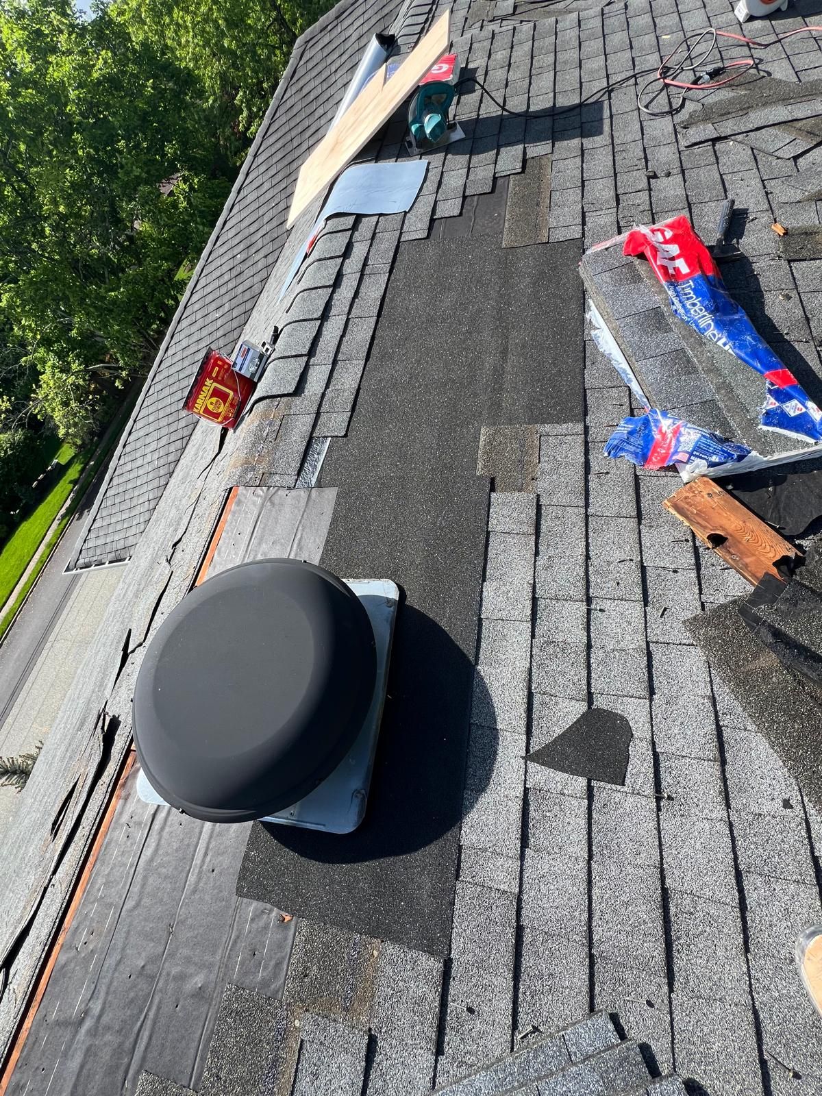 Rooftop with missing shingles, vent, and debris. Work in progress on a gray shingle roof.