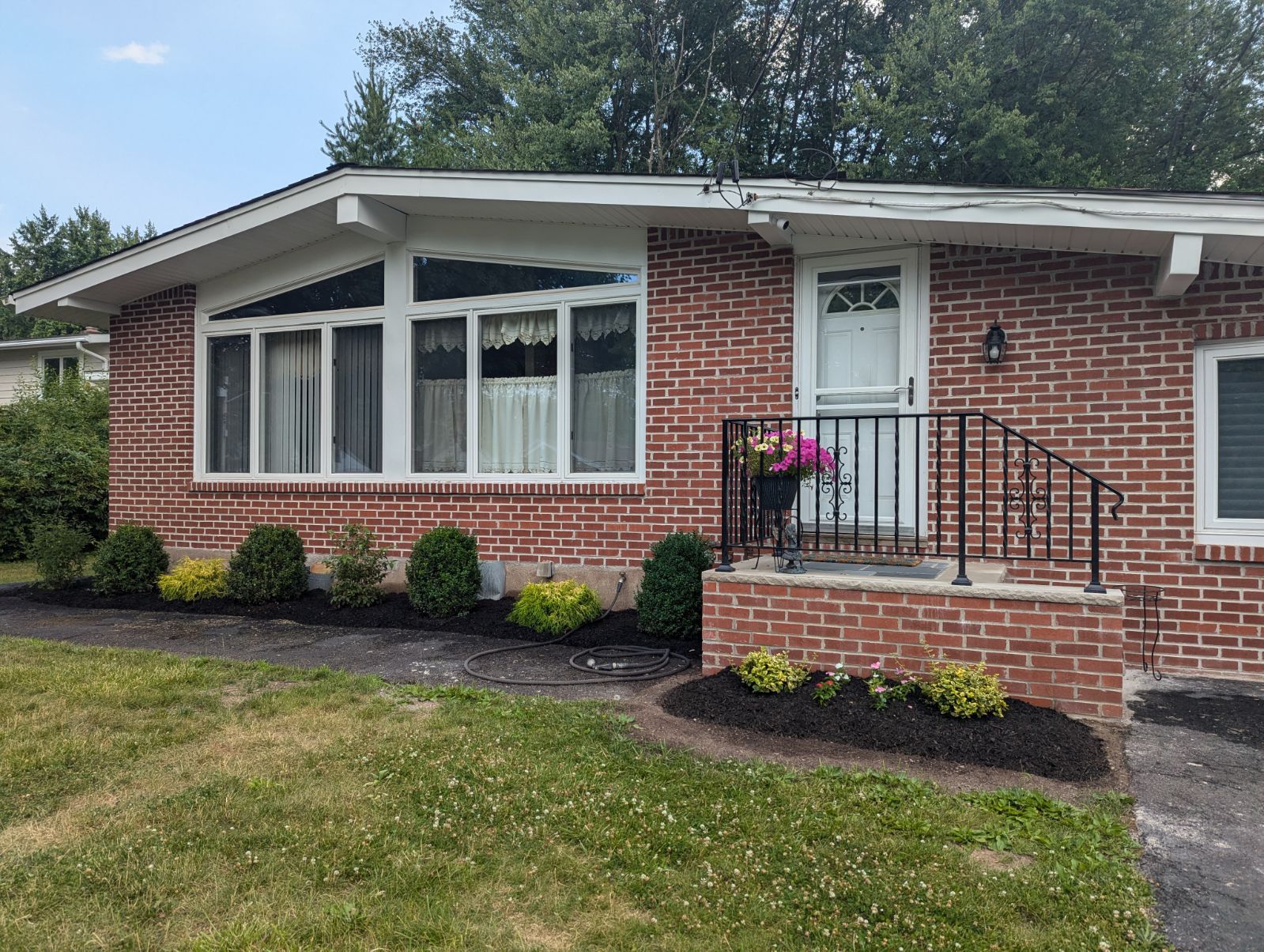 Red brick house with white trim, a small porch, and landscaping; sunny day.