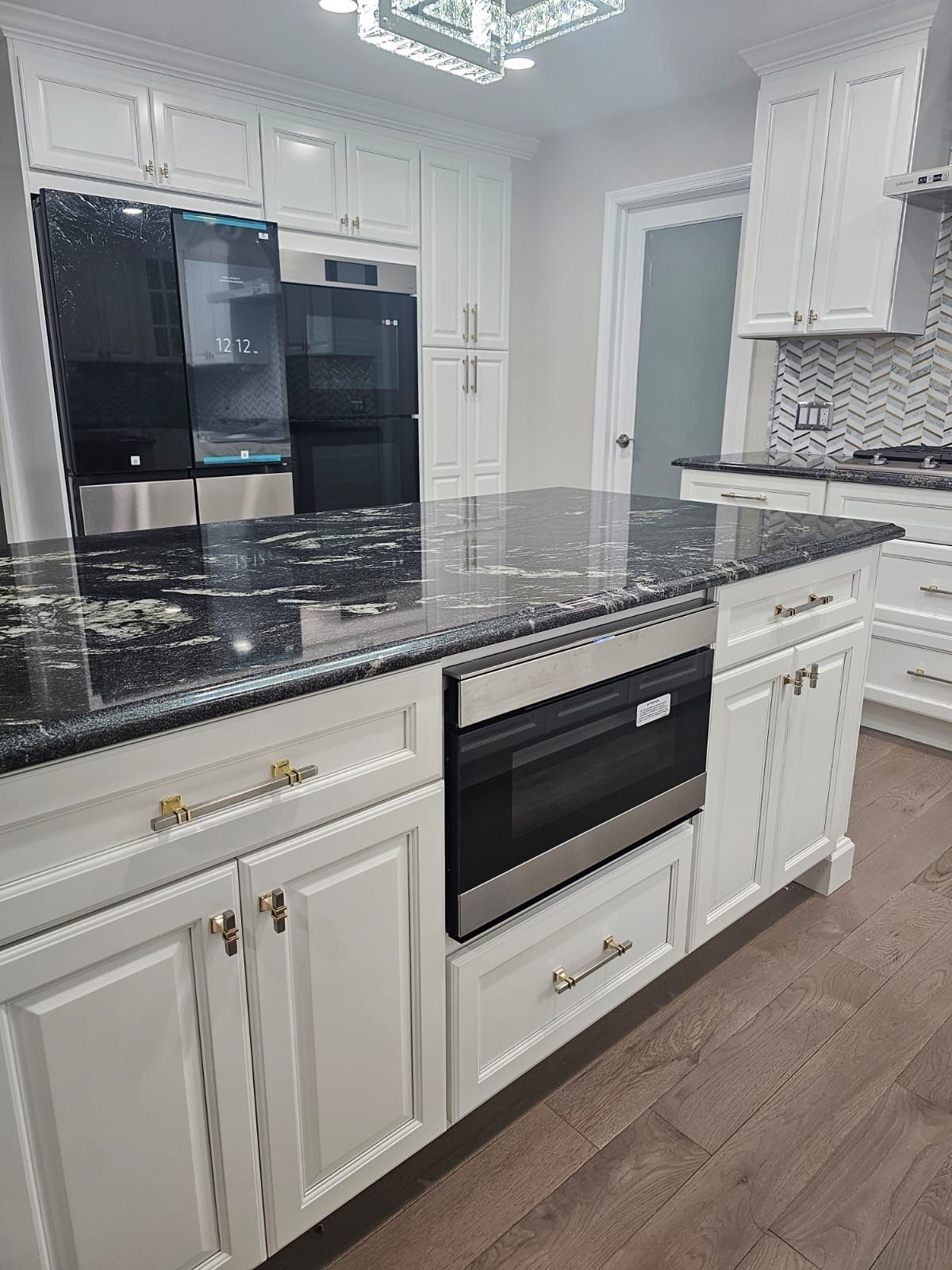 White kitchen with black countertops, stainless steel appliances, and wooden floors.