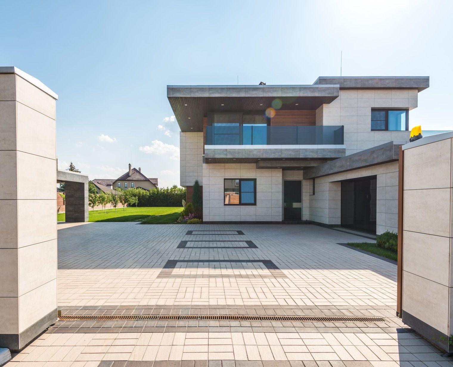 Modern two-story house with a brick driveway, open gate, and blue sky.