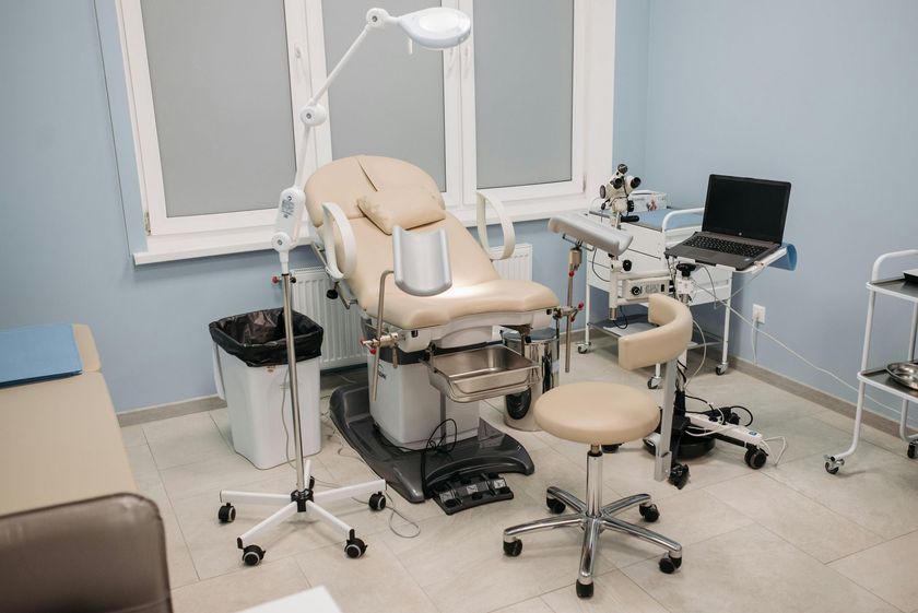 A medical examination room featuring a gynecological chair, a doctor's stool, diagnostic equipment, and a laptop.
