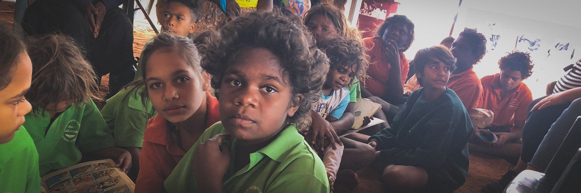 Several JPP School students sitting crossed legged on the ground