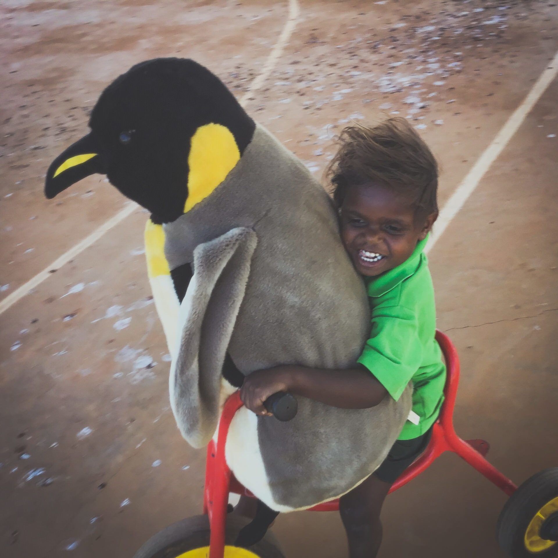 JPP School kindy student rying a tricycle while holding a large penguin