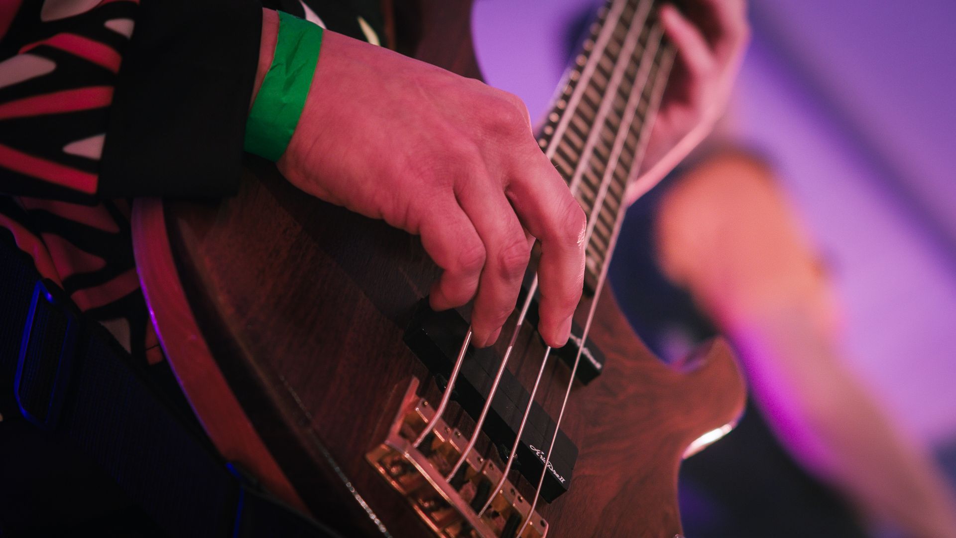 En person spiller en bassgitar med et grønt armbånd på håndleddet.