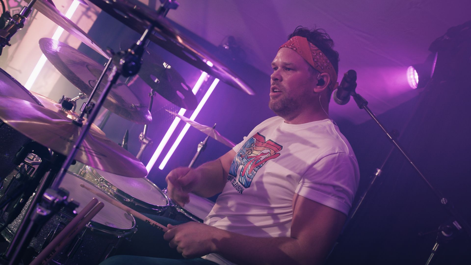 En mann spiller trommer på en scene i et mørkt rom.