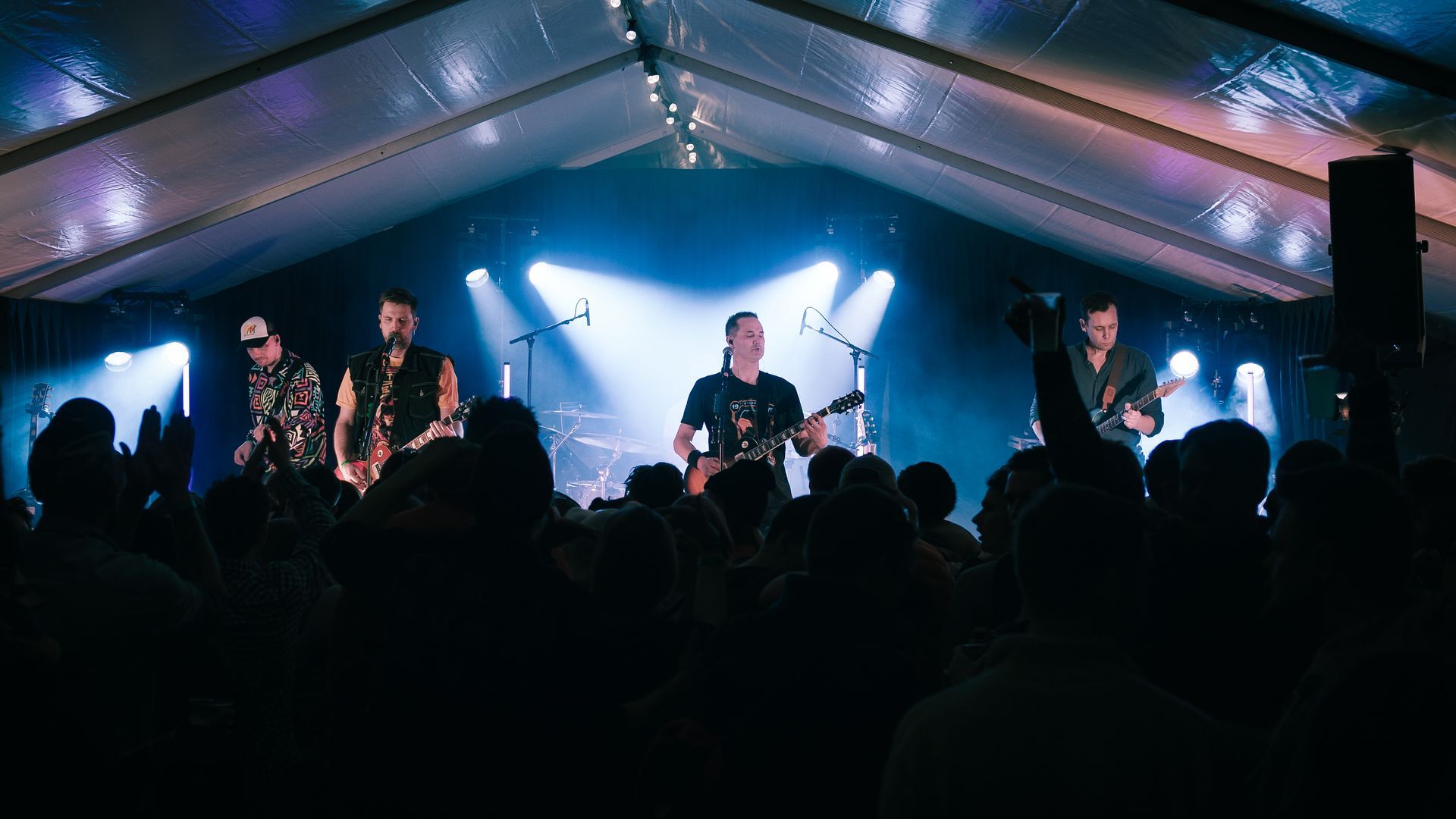 En gruppe menn spiller instrumenter på en scene foran en folkemengde.