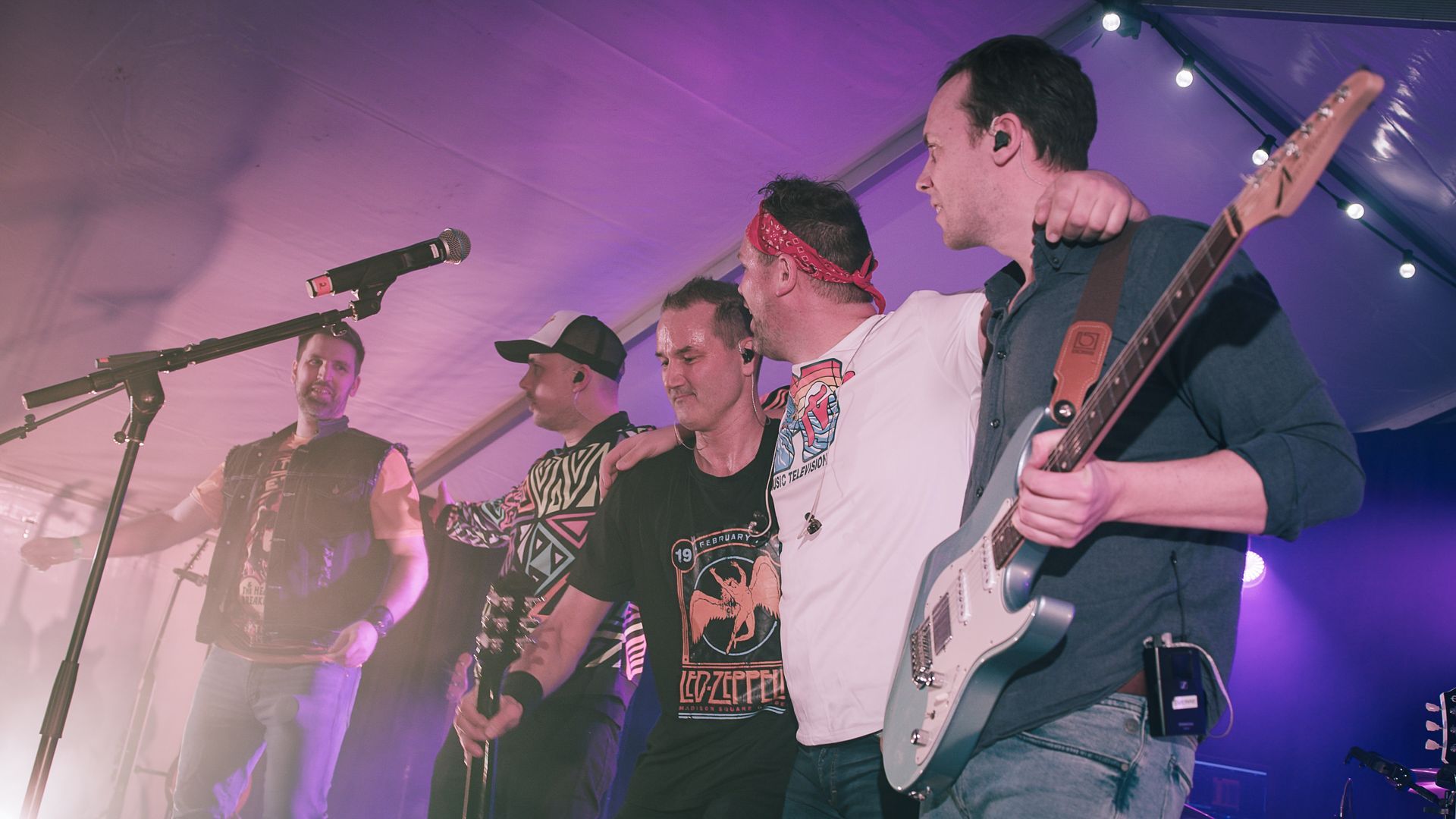 En gruppe menn står på en scene med gitarer og synger i mikrofoner.