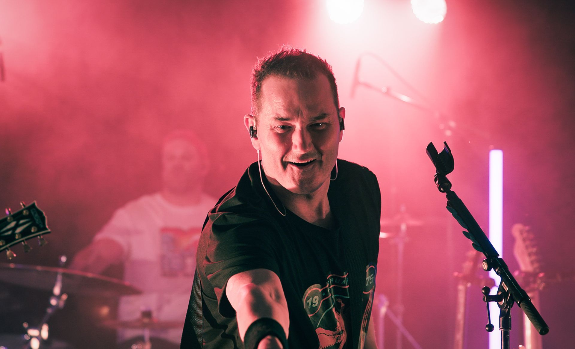 En mann spiller gitar på en scene foran en mikrofon.