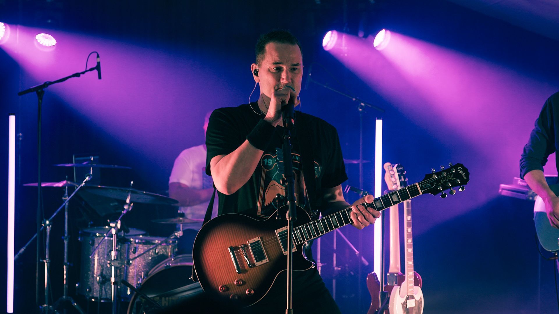 En mann spiller gitar og synger i en mikrofon på en scene.