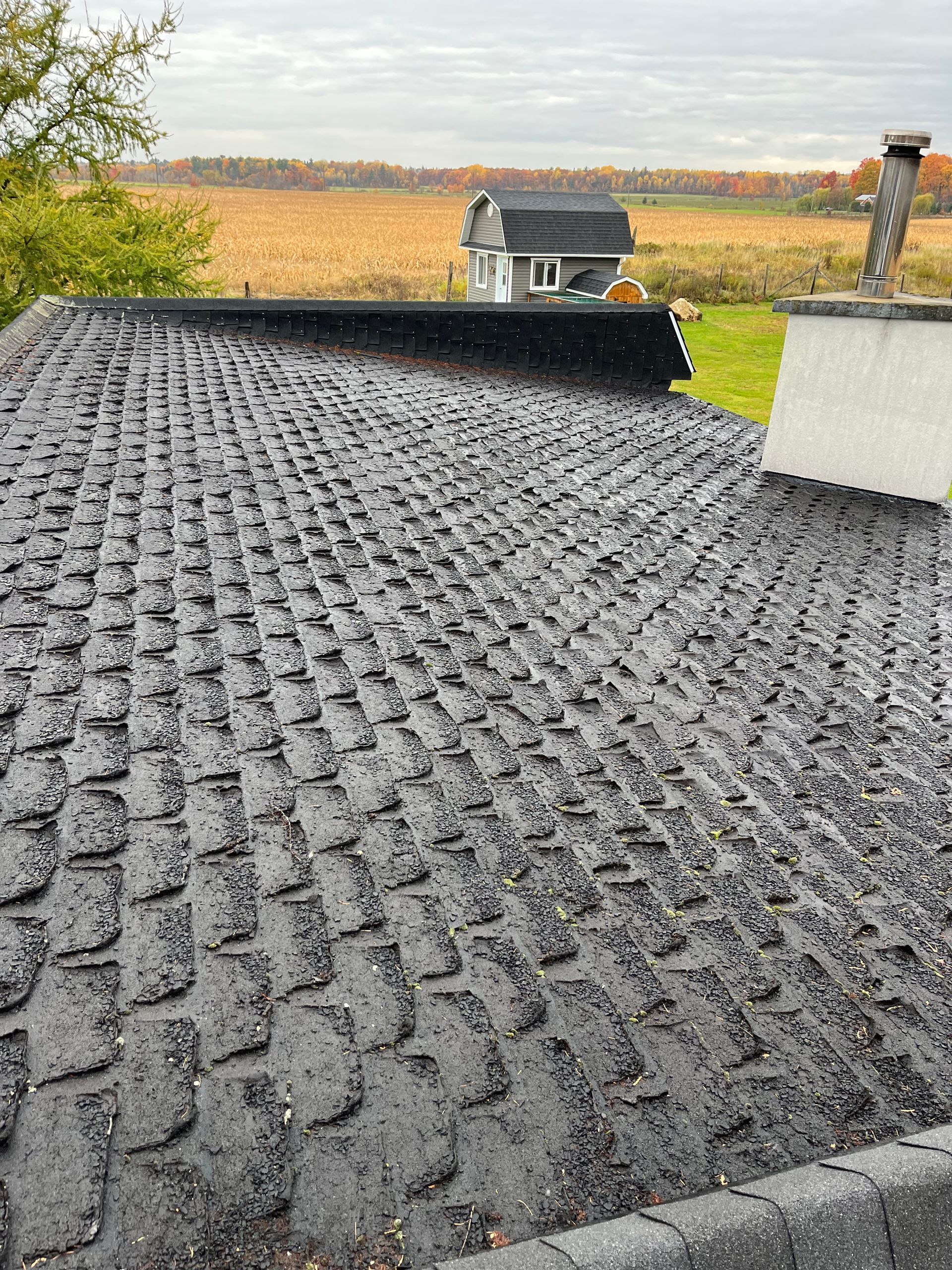 Un gros plan d'un toit avec une cheminée et une maison en arrière-plan.