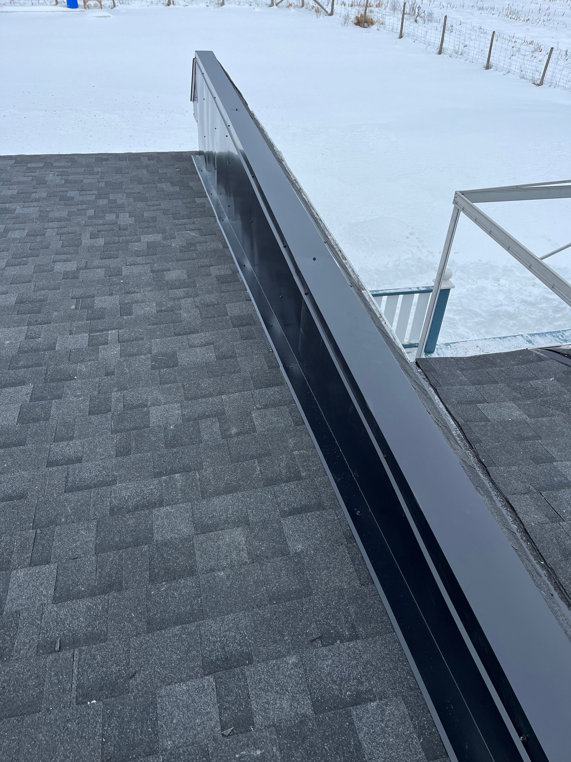 Une balustrade noire est posée au sommet d'un toit à côté d'un champ enneigé.