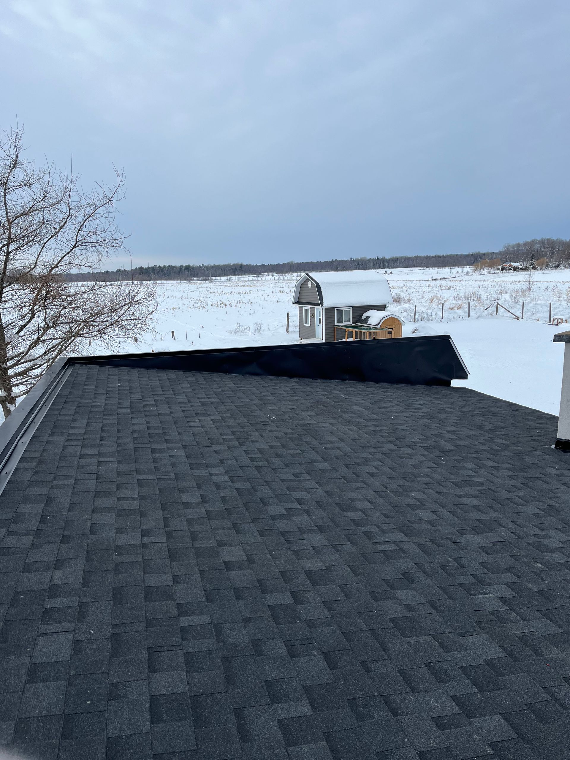 Un toit avec vue sur un champ enneigé et une maison en arrière-plan.