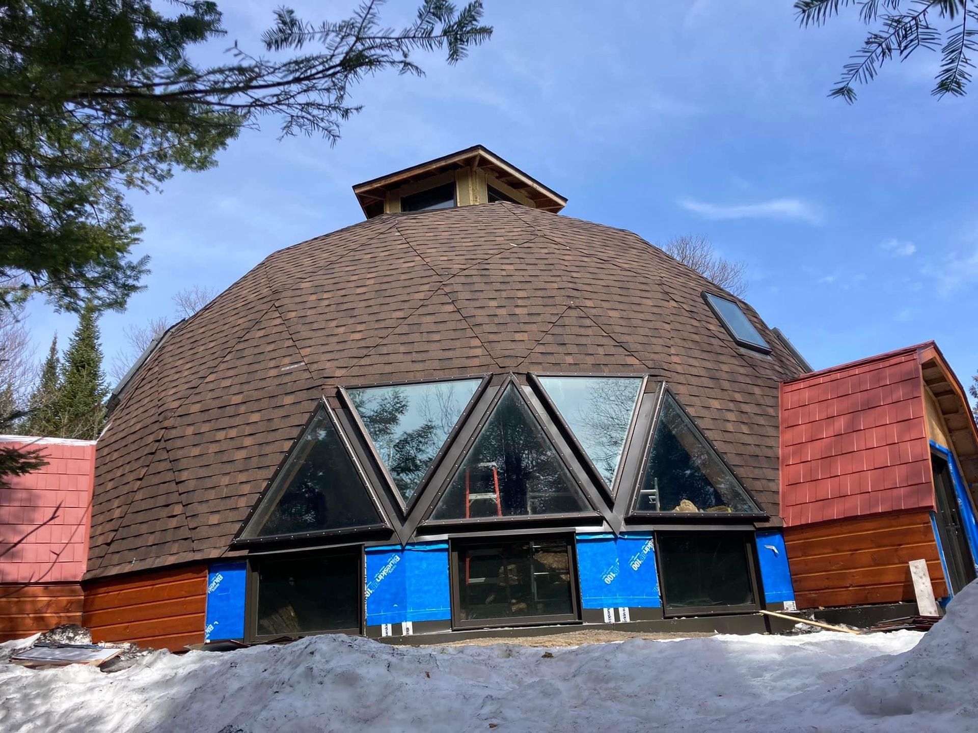 Un bâtiment en forme de dôme avec un toit rouge est entouré de neige et d'arbres.