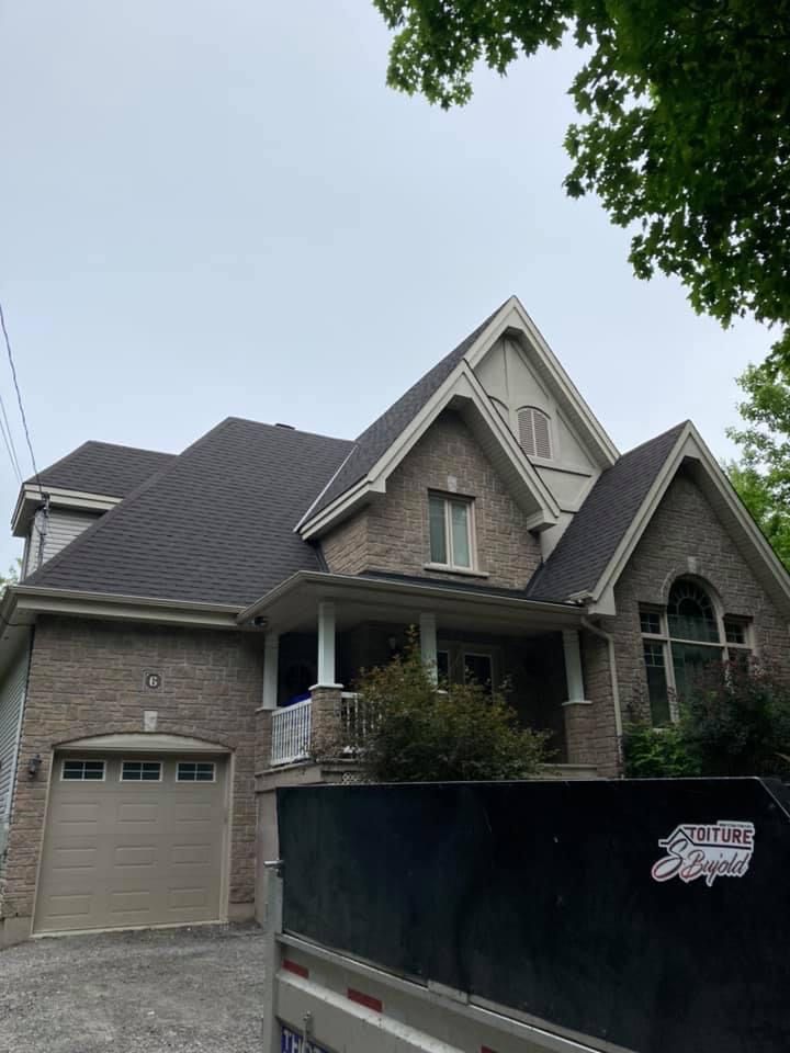 Une grande maison en briques avec un toit noir et un camion garé devant.