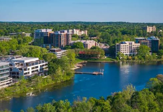Lakefront apartment buildings beside a calm blue lake with trees and a dock
