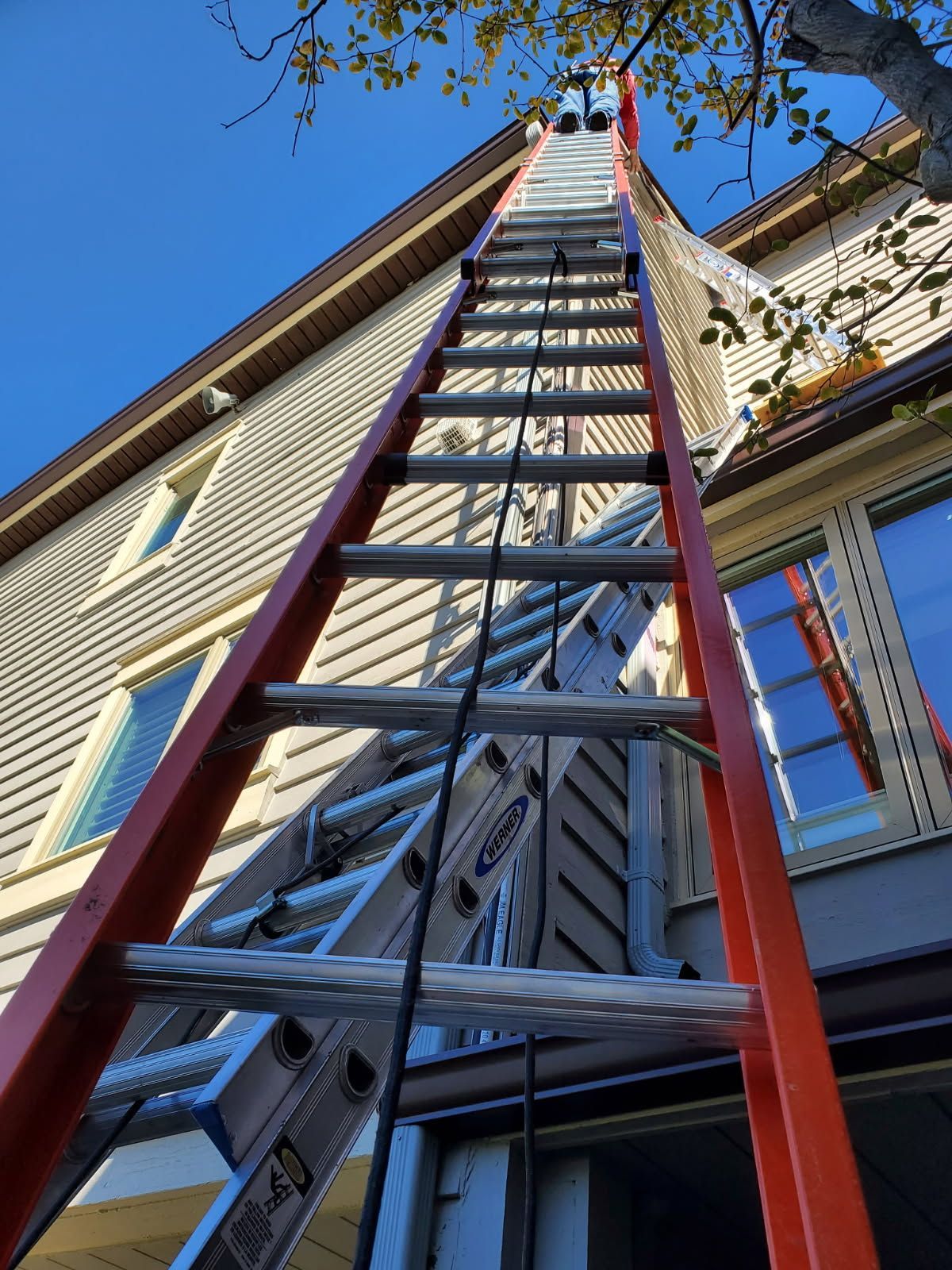 Ladder leaning against a house exterior, reaching up to the roofline under a blue sky