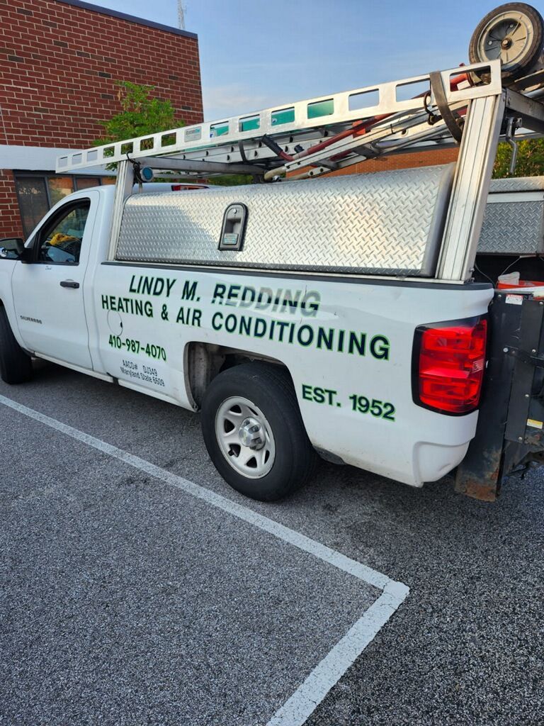 White HVAC service truck with ladder racks and company signage parked in a lot