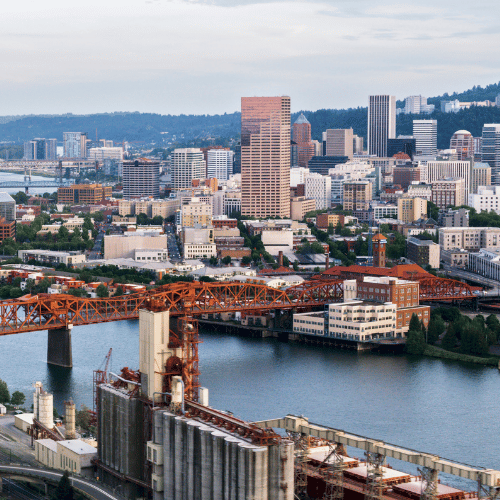 Portland, Oregon skyline with a bridge over the Willamette River. Includes tall buildings and industrial structures.