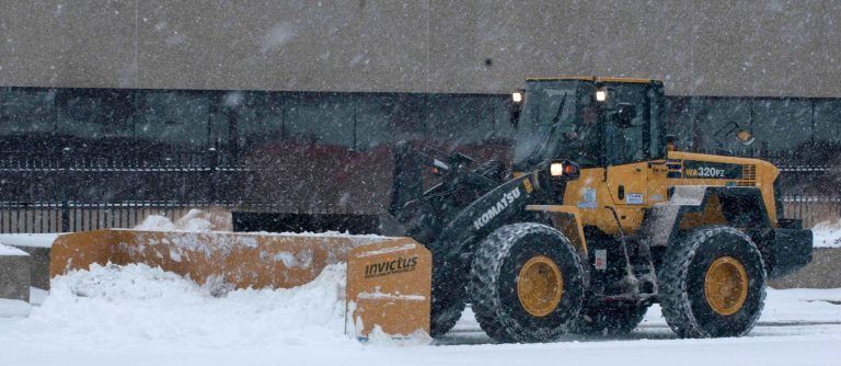 Yellow snowplow clearing snow. Snow is falling.