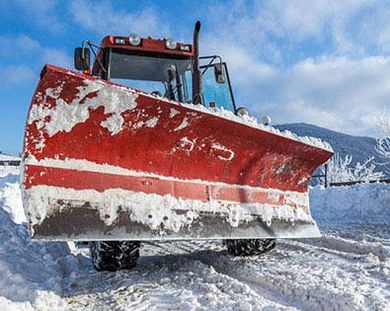 Red snowplow on snowy road, clearing snow under a blue sky.