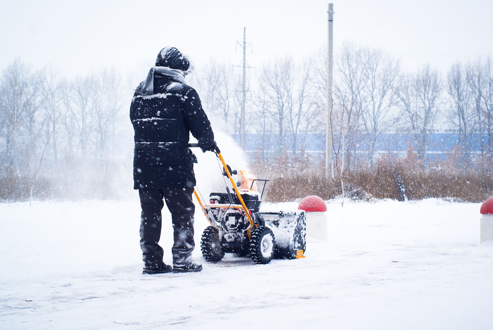 Person in black coat using a yellow snowblower in a snowy area.