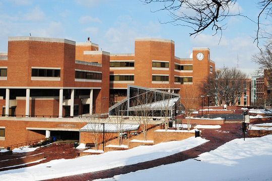 Brick university building in winter with snow on the ground. Glass bridge connects buildings.