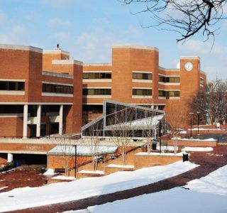 Brick university building with snow, clock tower, and glass entrance.