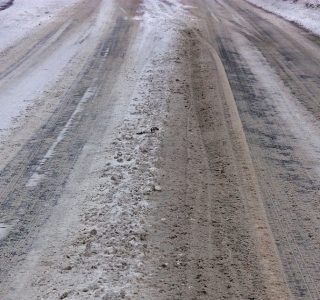 Snowy road, showing tire tracks and slush in a winter landscape.
